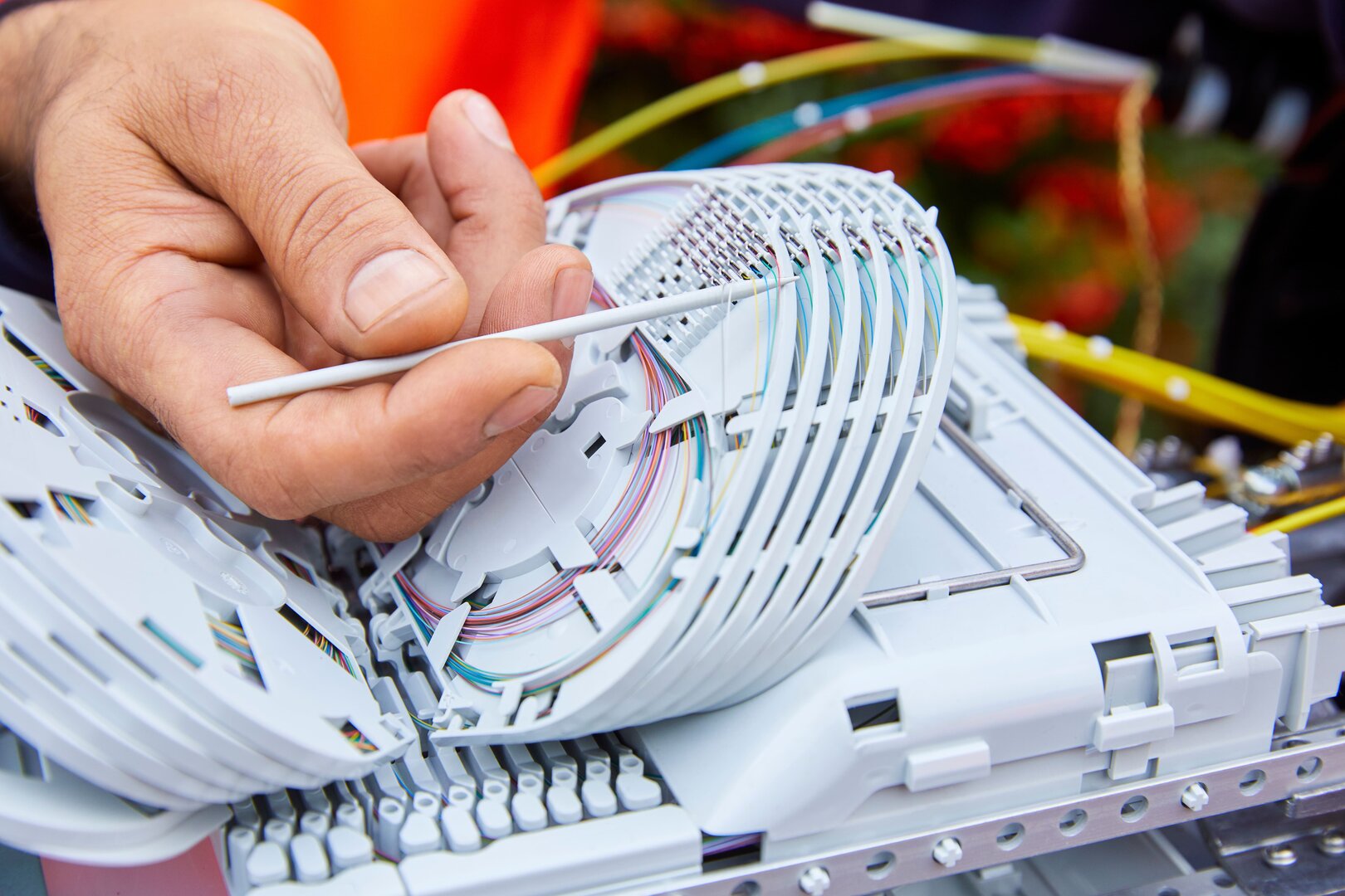 Techniker arbeitet an einem Glasfaserspleißkasten und führt einzelne Fasern in die Halterungen ein.