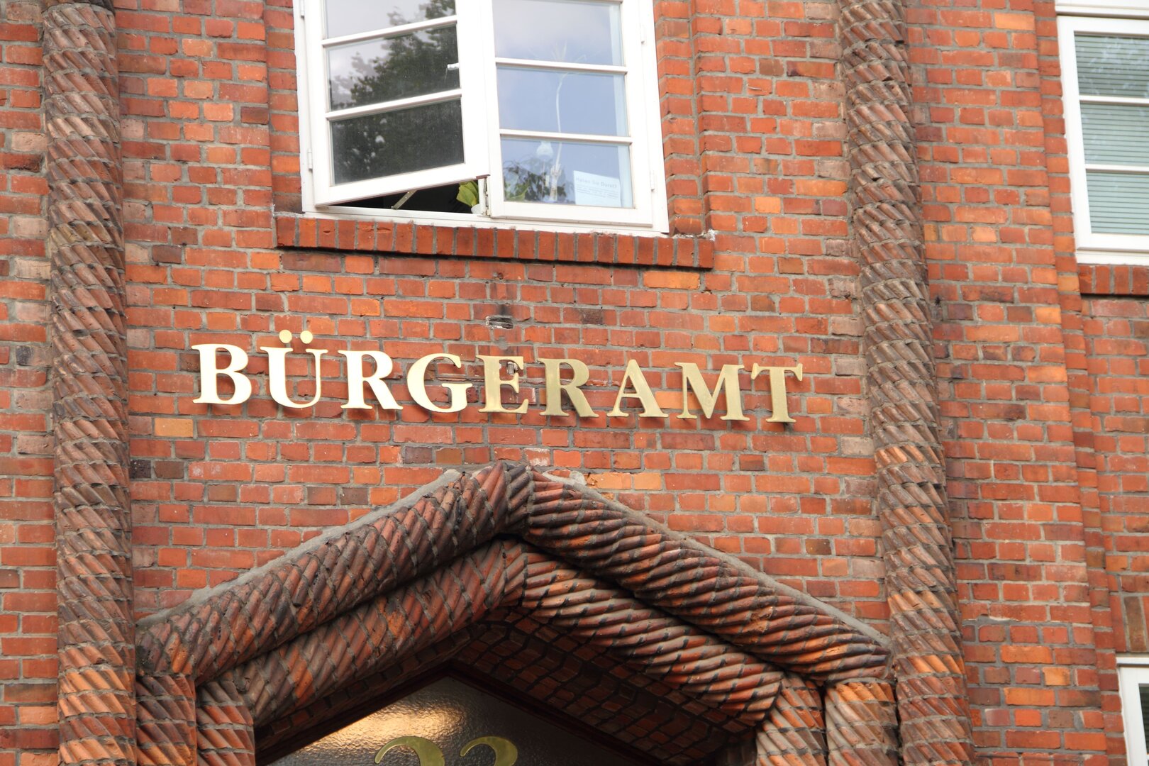 Eingangsbereich eines Bürgeramts mit goldfarbener Beschriftung an einer Backsteinfassade