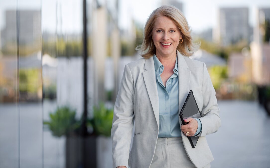 businessfrau -tablet-aussenbereich Geschäftsfrau geht lächelnd im Außenbereich eines Bürokomplexes und hält ein Tablet in der Hand.